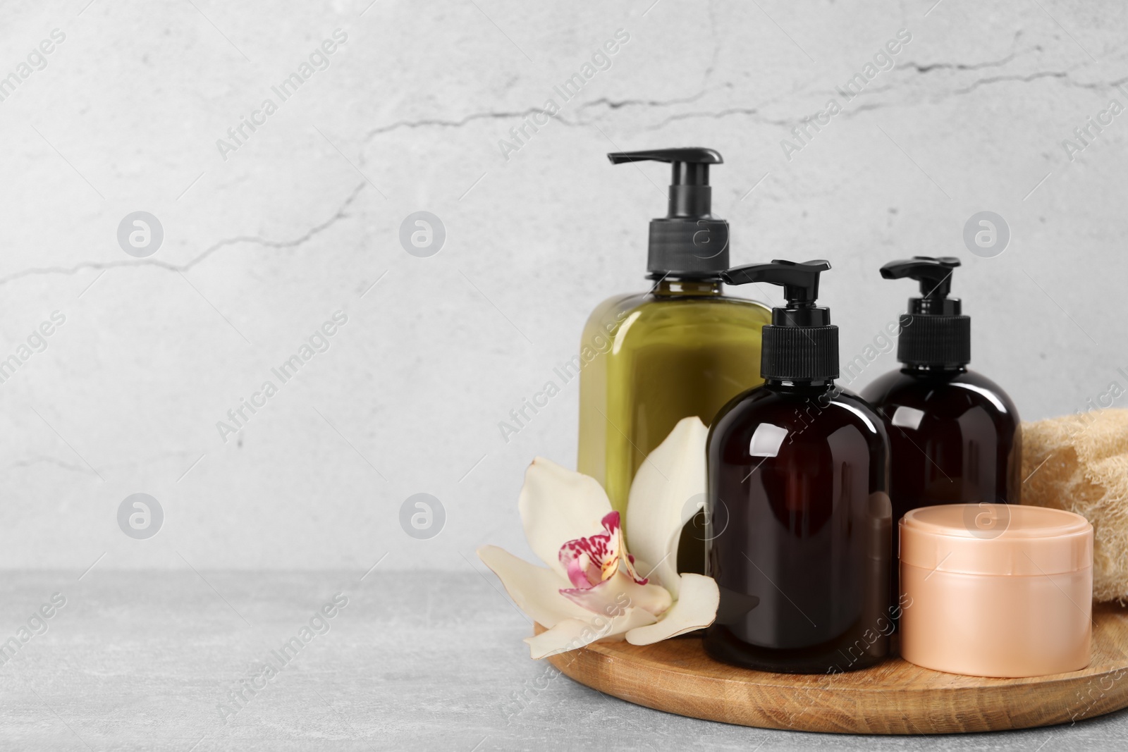 Photo of Shampoo bottles, hair mask, loofah and orchid flower on light grey table, space for text