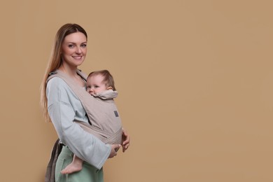 Mother holding her child in sling (baby carrier) on light brown background. Space for text