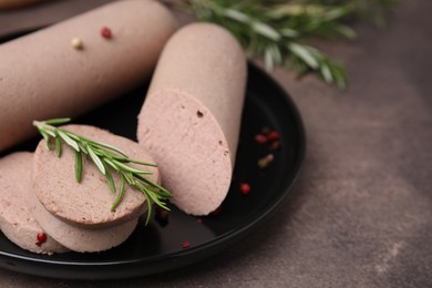 Photo of Delicious liver sausages with rosemary on brown textured table, closeup. Space for text