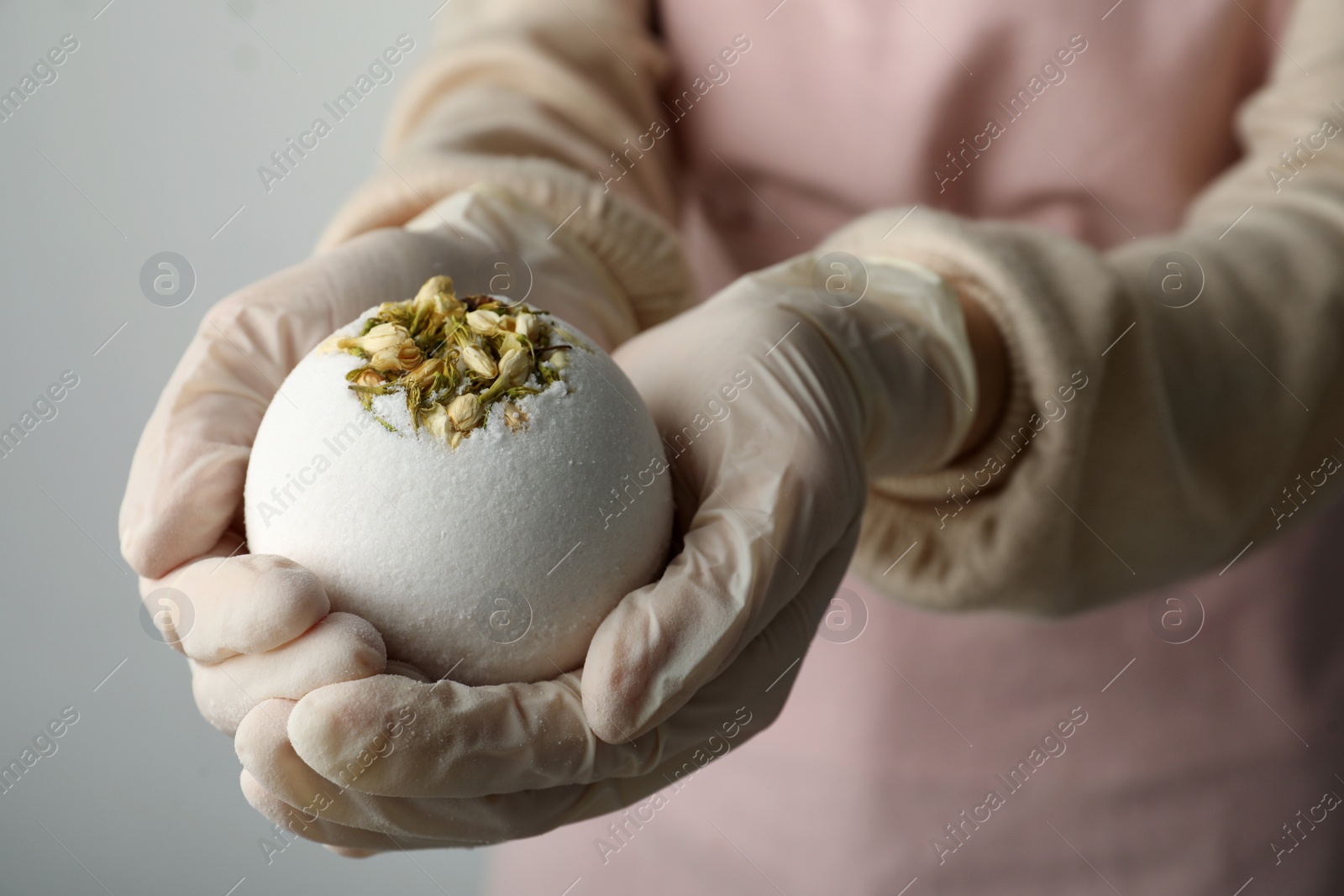 Photo of Woman in gloves with self made bath bomb on light grey background, closeup