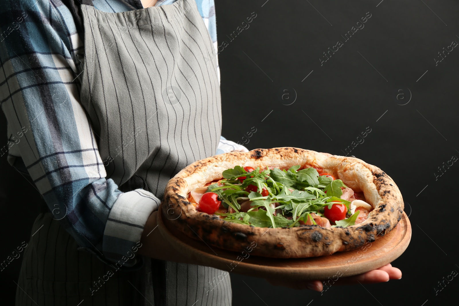 Photo of Woman holding tasty pizza with meat and arugula on black background, closeup