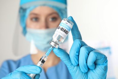 Doctor filling syringe with vaccine against Covid-19 indoors, focus on hands