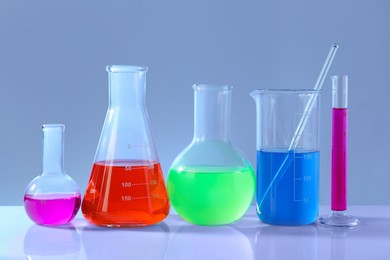 Different laboratory glassware with colorful liquids on white table against grey background