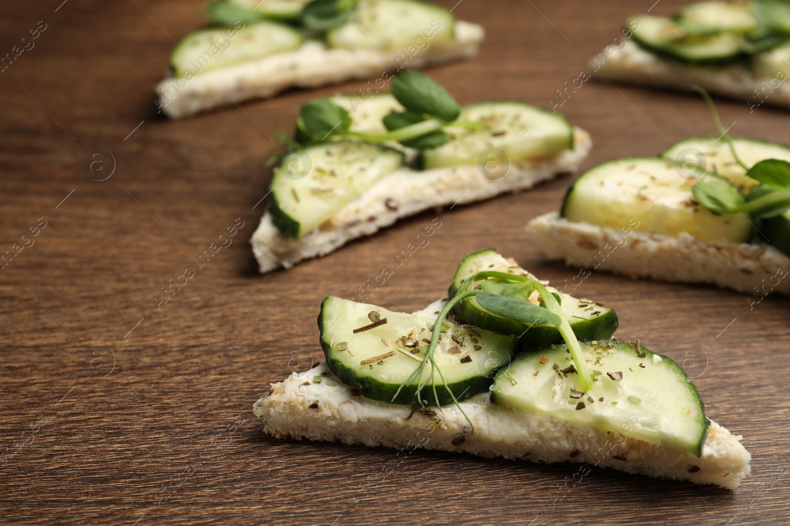Photo of Tasty sandwiches with cream cheese, cucumber and microgreens on wooden table, closeup
