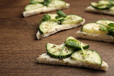 Tasty sandwiches with cream cheese, cucumber and microgreens on wooden table, closeup