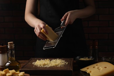 Photo of Woman grating cheese at wooden table, closeup