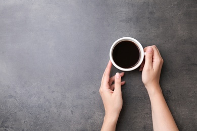 Photo of Young woman with cup of delicious hot coffee on grey background, top view