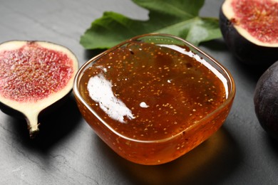 Photo of Glass bowl with tasty sweet jam, fresh figs and green leaf on grey table, closeup