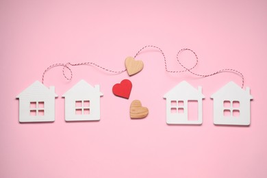 Photo of Decorative hearts and cord between white house models on pink background symbolizing connection in long-distance relationship, flat lay
