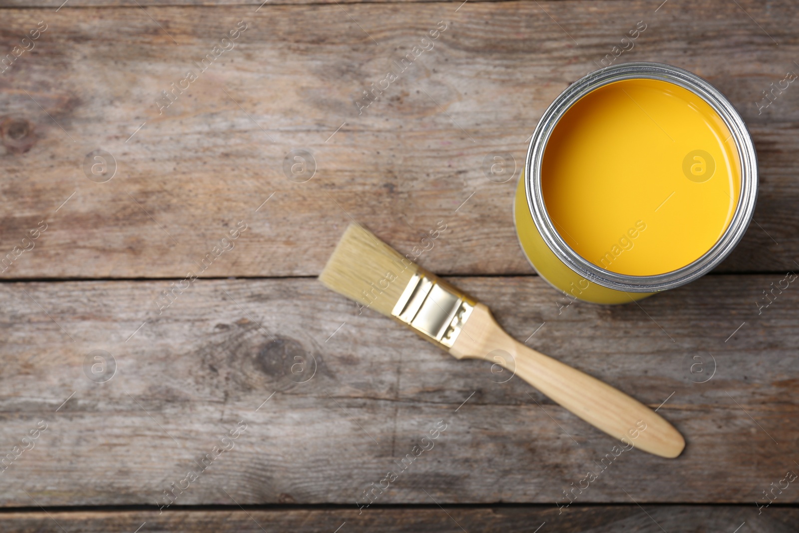 Photo of Can with yellow paint and brush on wooden background, top view. Space for text