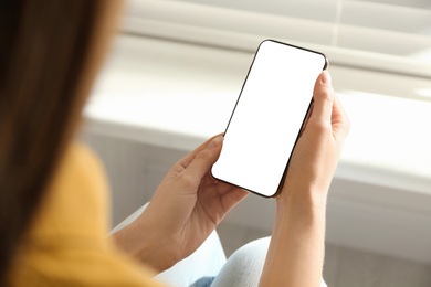 Young woman holding mobile phone with empty screen in hands indoors, closeup