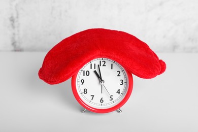 Photo of Red sleep mask and alarm clock on white table