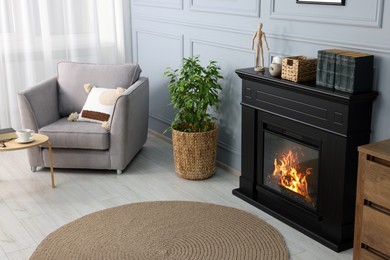 Black stylish fireplace near potted plant and armchair in cosy living room