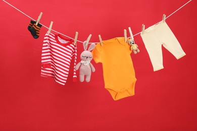 Different baby clothes and toys drying on laundry line against red background