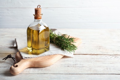 Photo of Wooden board with bottle of fresh rosemary oil on table