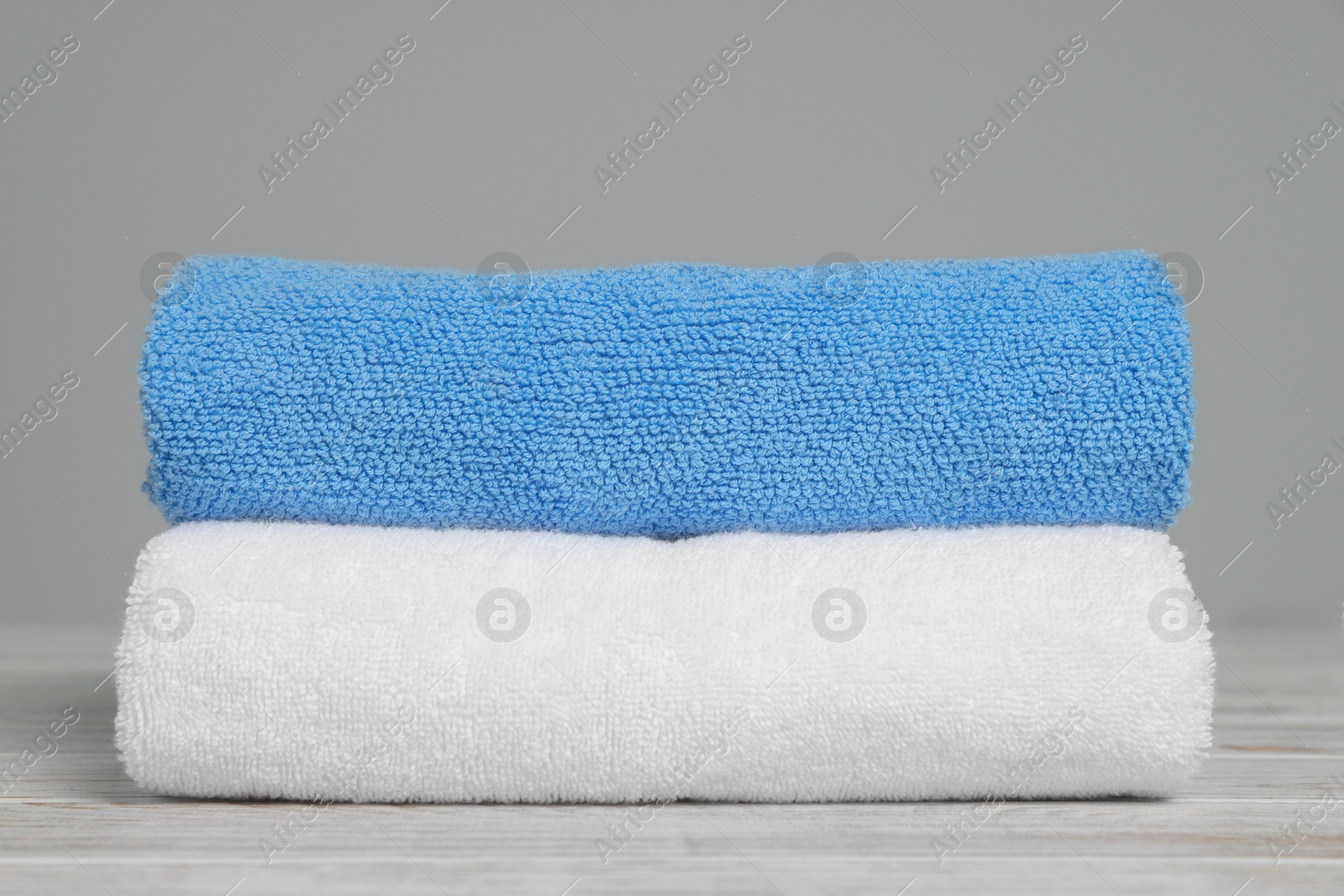 Photo of Soft folded towels on white wooden table against light grey background