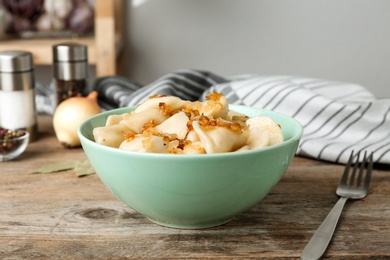 Photo of Delicious cooked dumplings with fried onion on wooden table