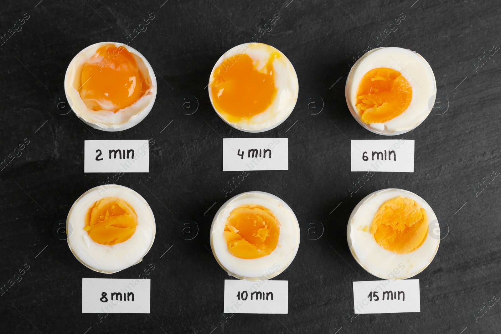 Photo of Different cooking time and readiness stages of boiled chicken eggs on black table, flat lay