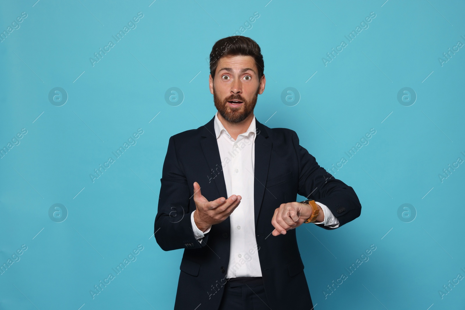 Photo of Emotional man checking time on light blue background. Being late concept