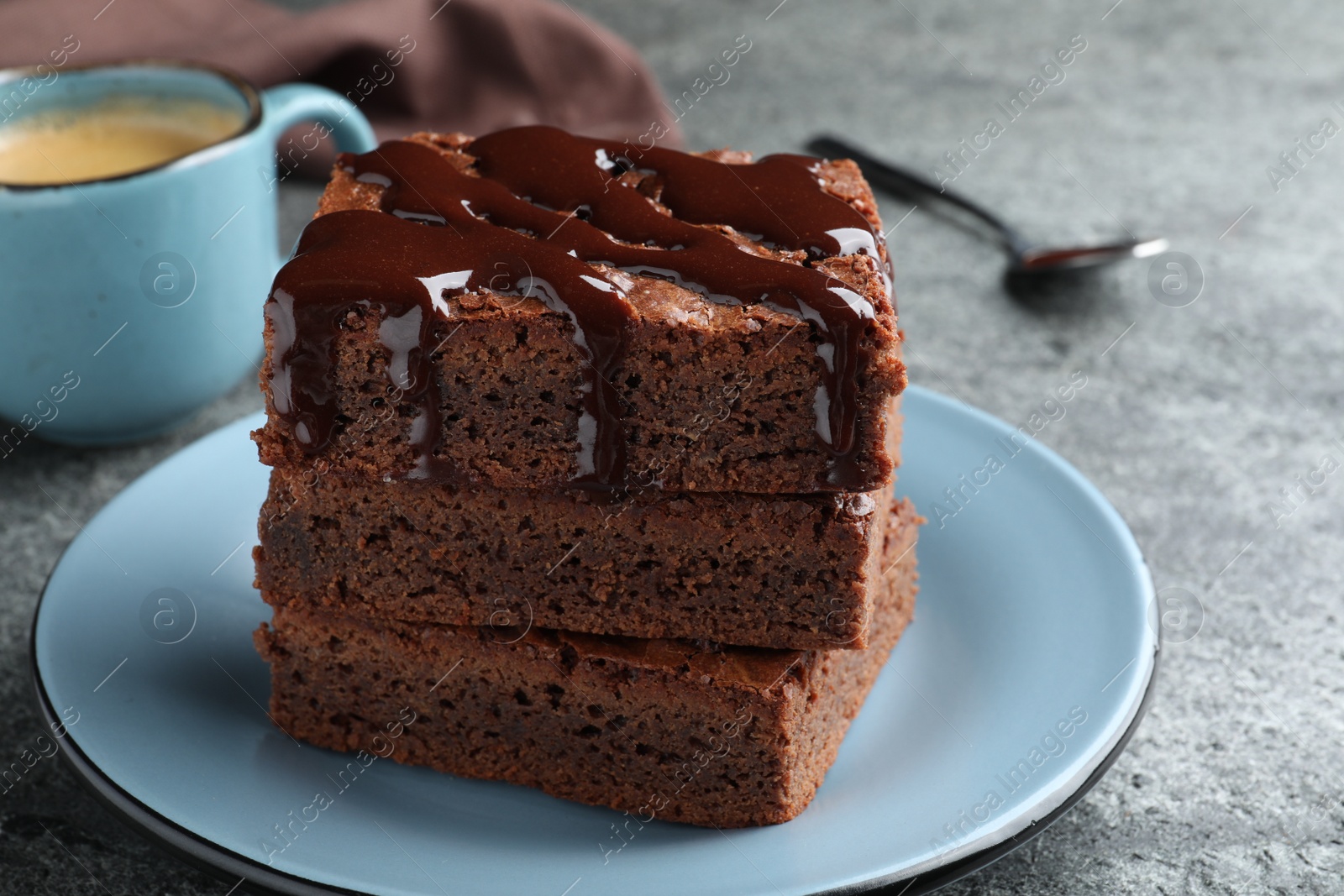 Photo of Delicious chocolate brownies with sweet syrup served on grey table