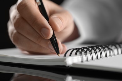 Photo of Man writing in notebook at black table, closeup