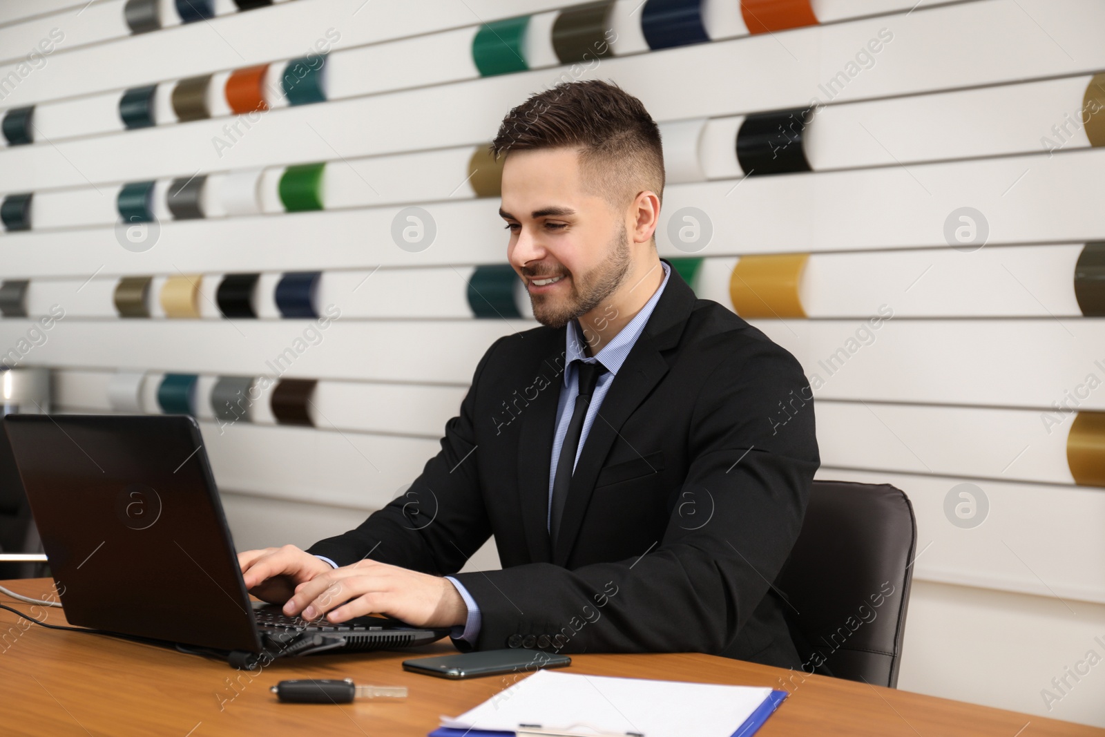 Photo of Salesman working with laptop at desk in car dealership