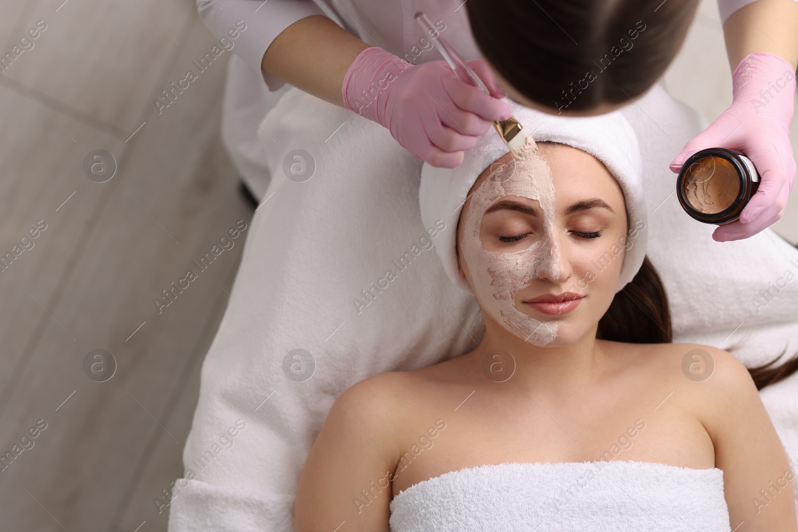 Photo of Cosmetologist applying mask on woman's face in clinic, top view. Space for text