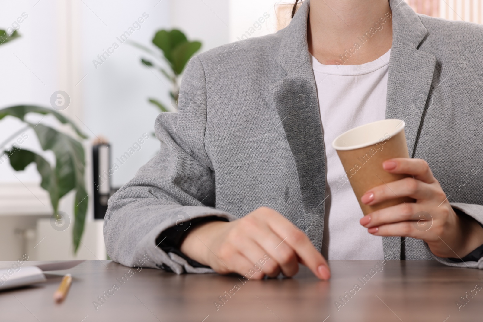 Photo of Woman showing stain from coffee on her jacket at wooden table indoors, closeup