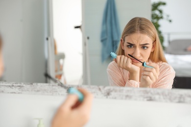 Photo of Young woman with eyelash loss problem applying mascara indoors