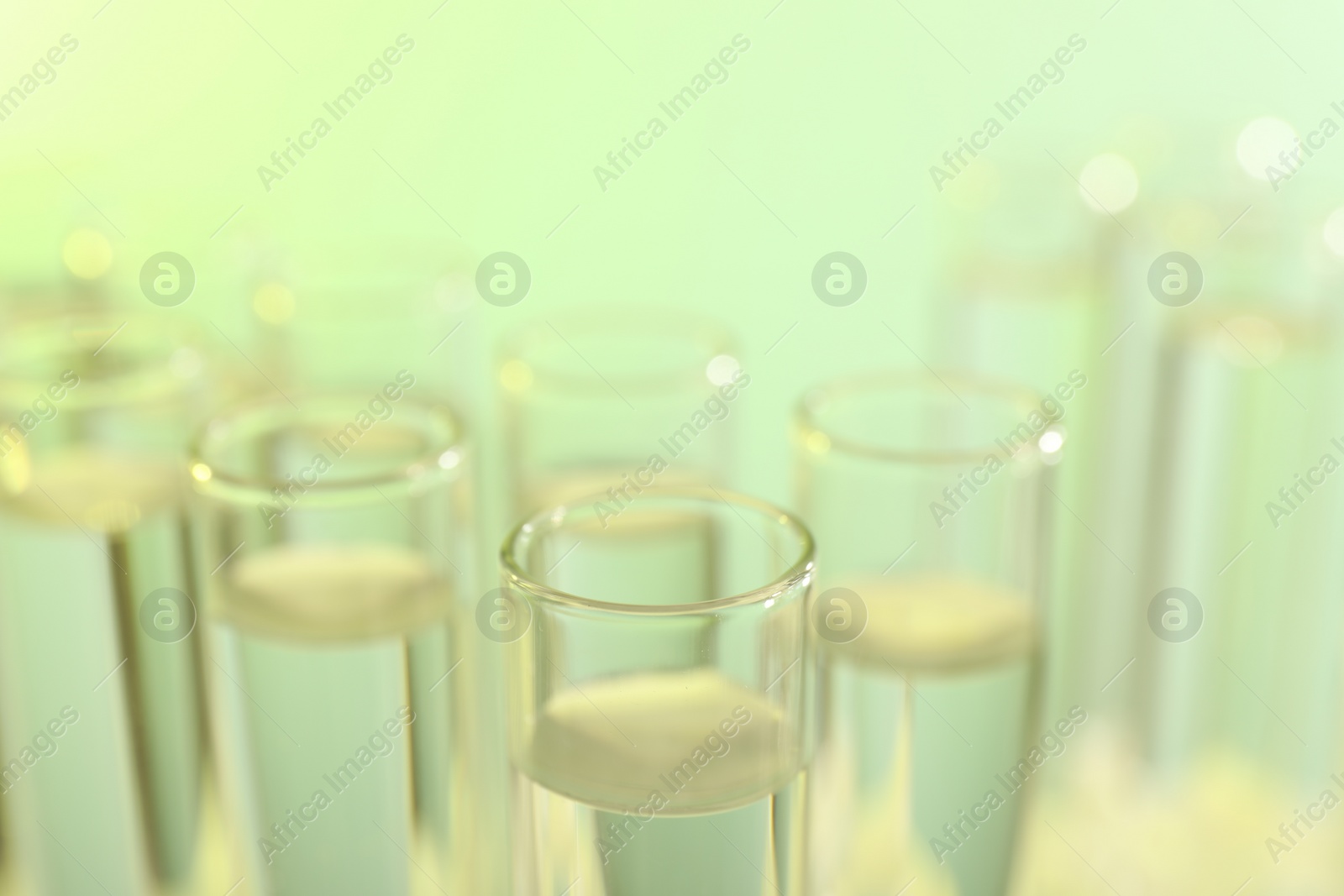 Photo of Many glass test tubes on yellow background, closeup