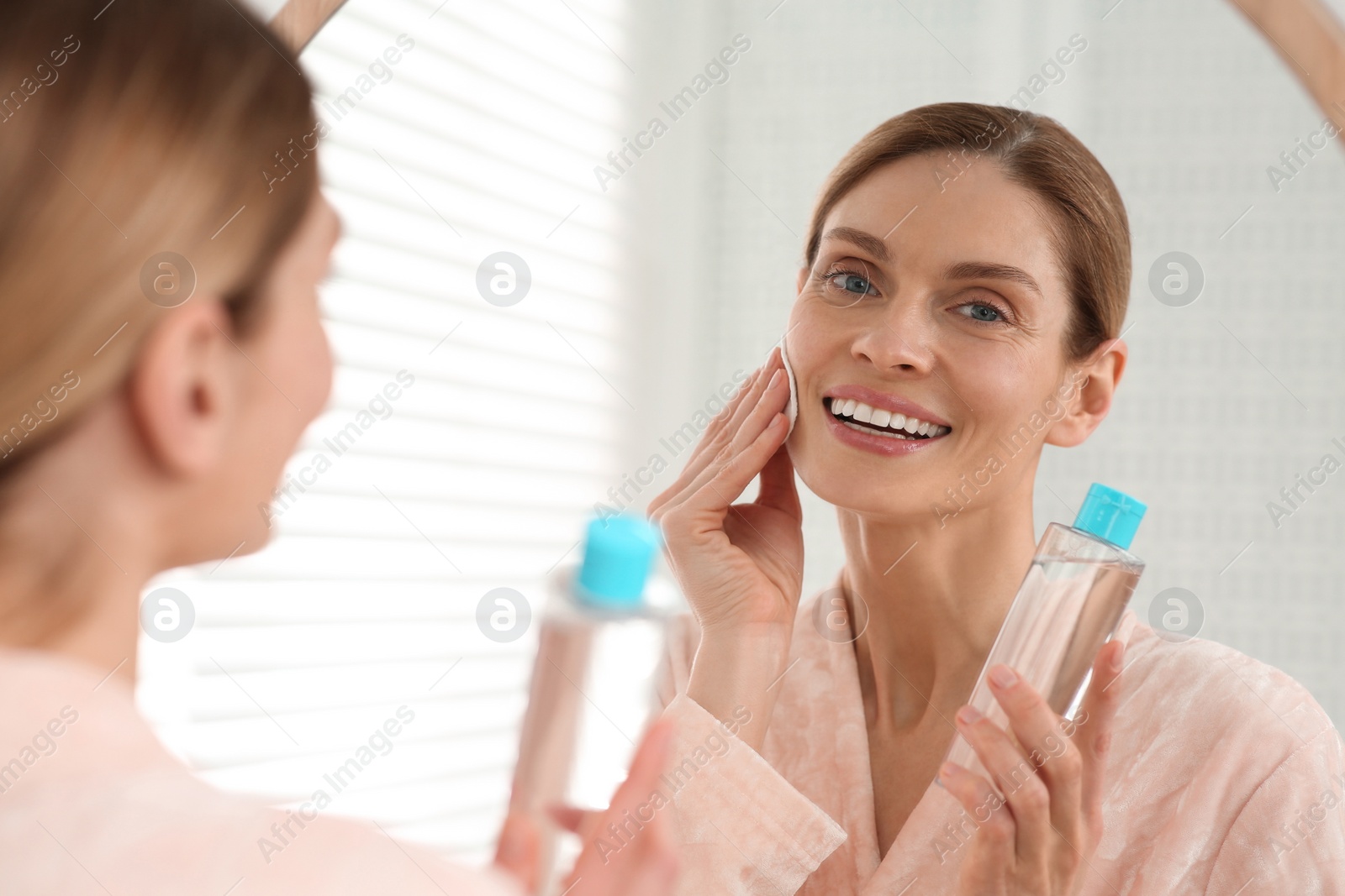 Photo of Beautiful woman removing makeup with cotton pad near mirror indoors