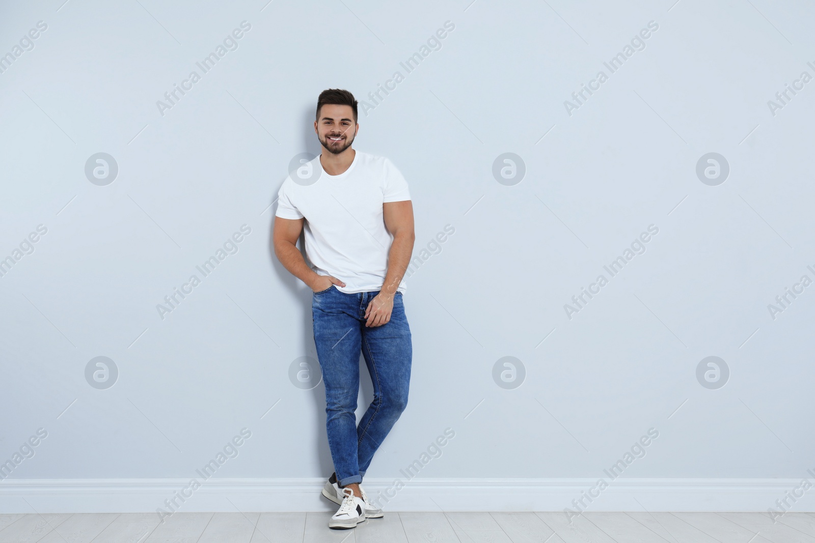 Photo of Young man in stylish jeans near light wall