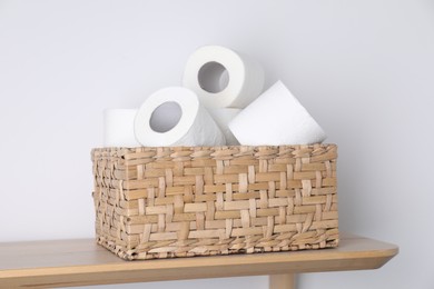 Toilet paper rolls in wicker basket on wooden table near white wall