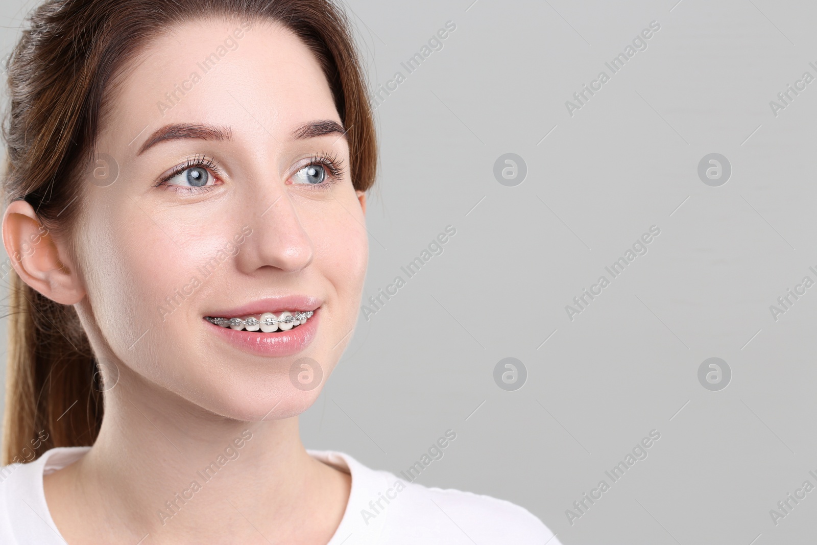 Photo of Portrait of smiling woman with dental braces on grey background. Space for text