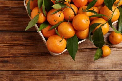 Photo of Fresh tangerines with green leaves in crate on wooden table, top view. Space for text