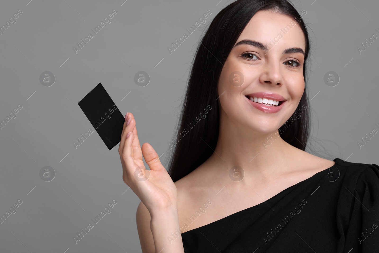 Photo of Happy woman holding blank business card on grey background. Space for text