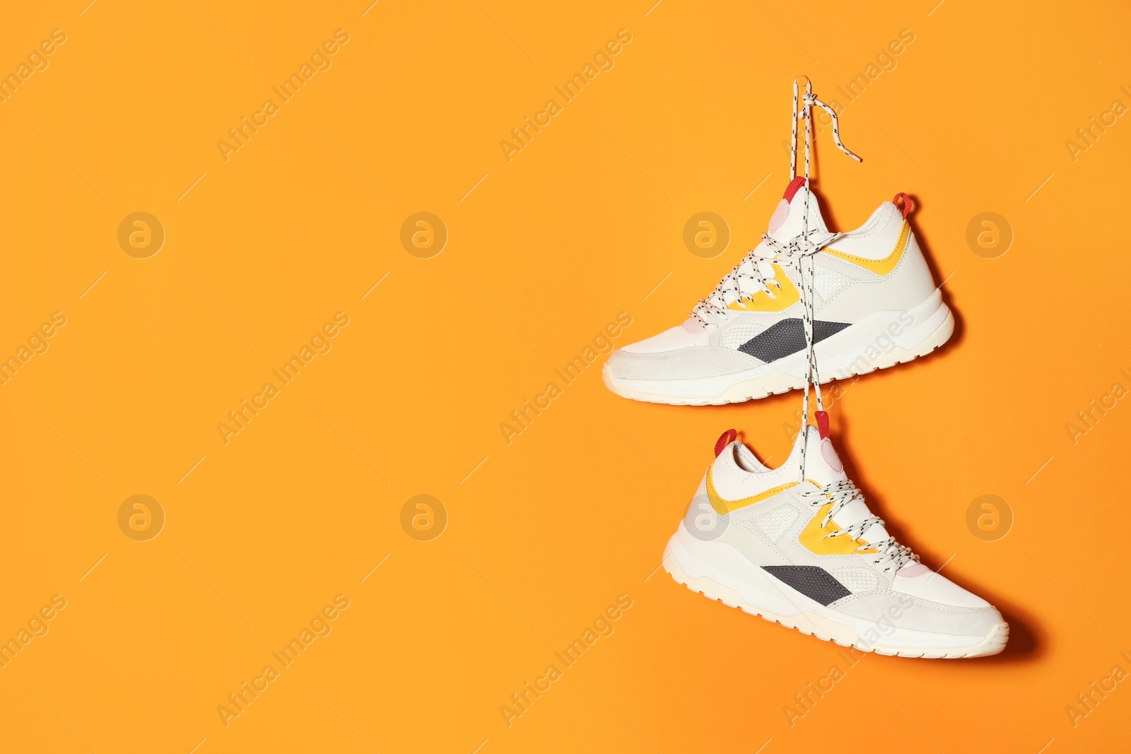 Photo of Pair of stylish sneakers hanging on color wall, space for text