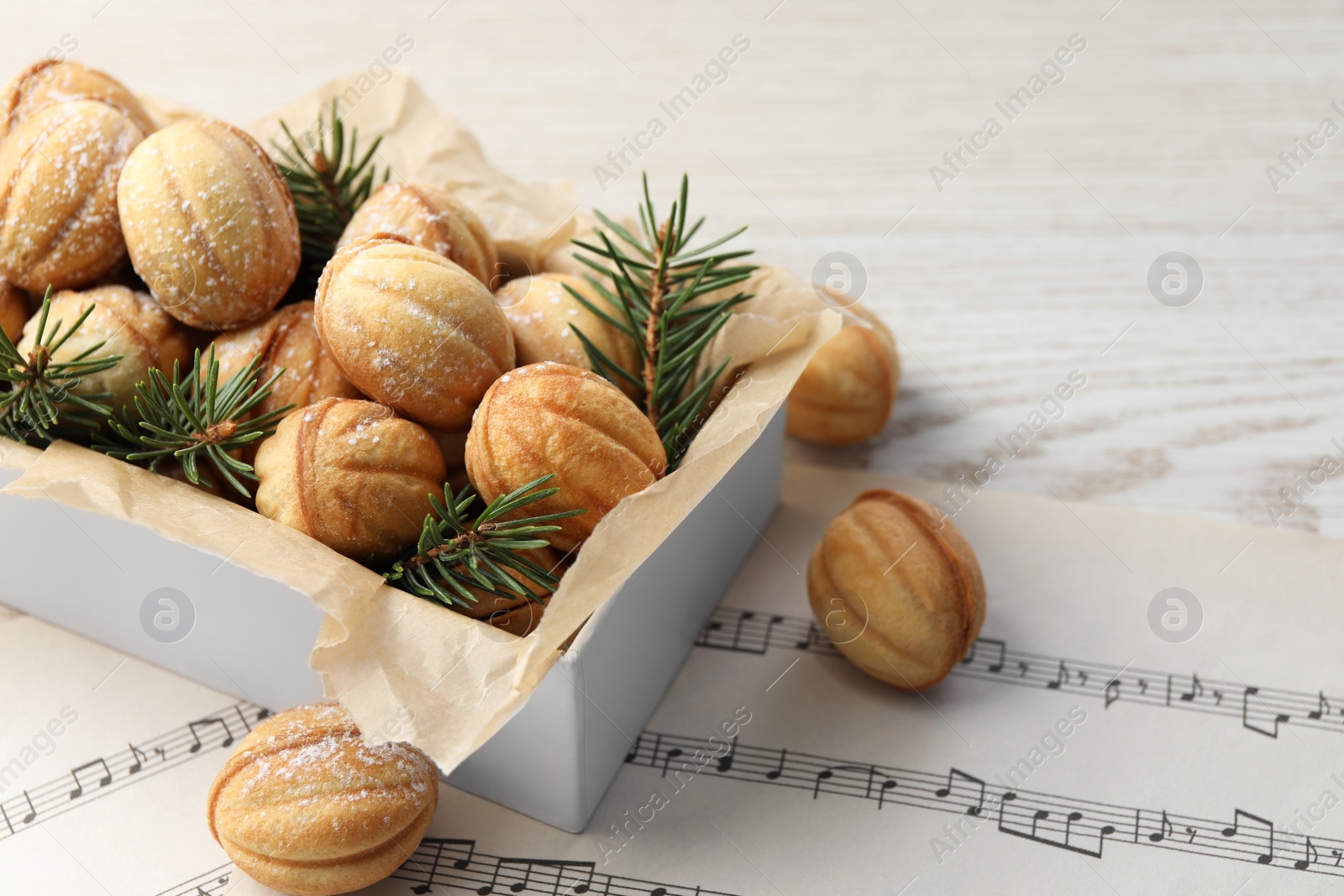 Photo of Homemade walnut shaped cookies and fir branches in box on white wooden table, space for text