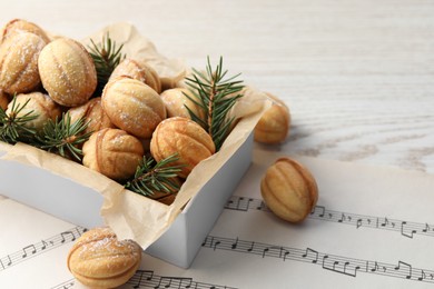 Photo of Homemade walnut shaped cookies and fir branches in box on white wooden table, space for text