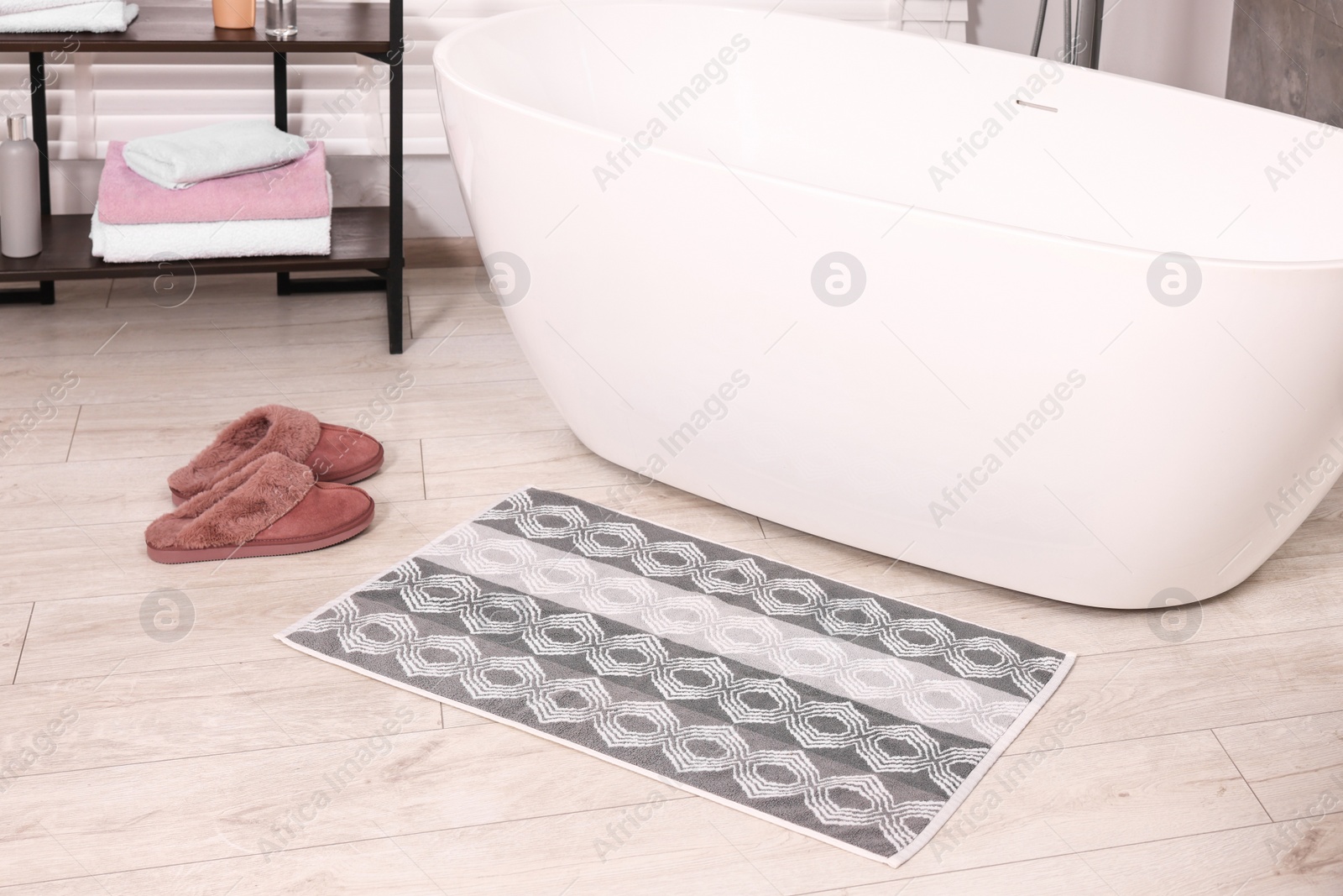 Photo of Soft bath mat with pattern and slippers near tub in bathroom