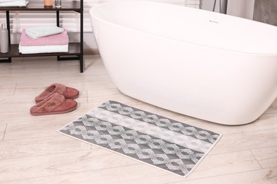 Soft bath mat with pattern and slippers near tub in bathroom