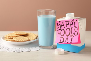 Photo of Glass of light blue milk, cookies and words Happy Fool's Day on wooden table