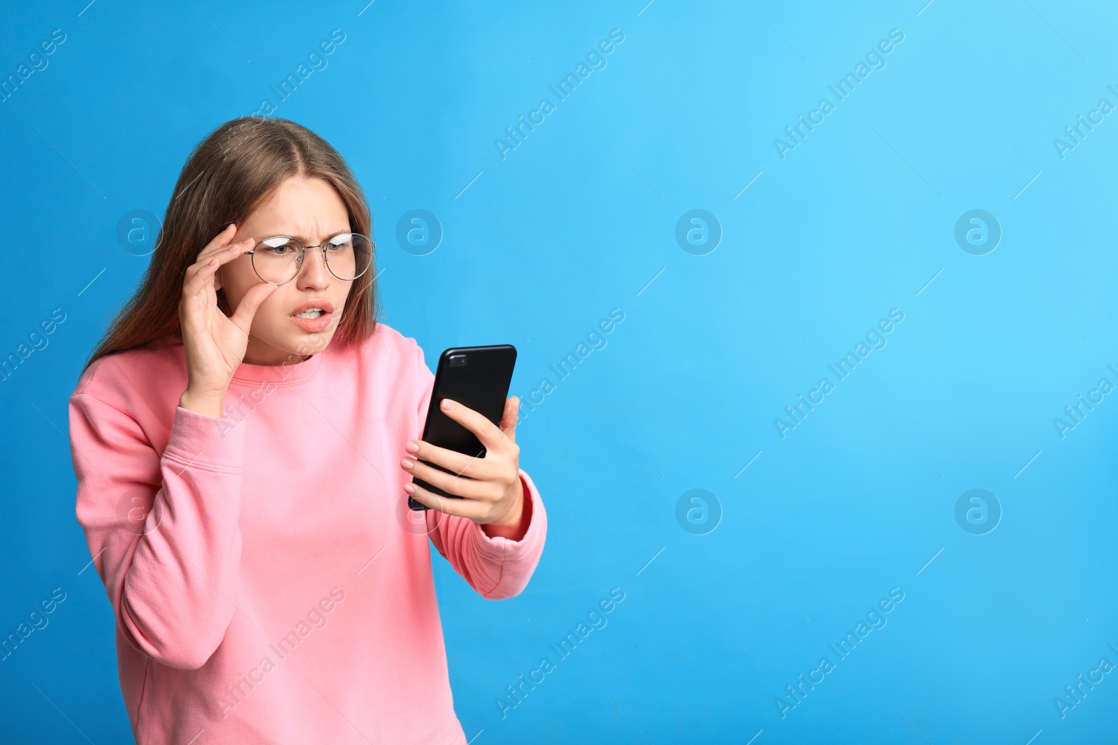 Photo of Young woman with vision problems using smartphone on blue background, space for text