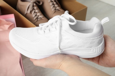 Woman holding stylish sport shoe indoors, closeup