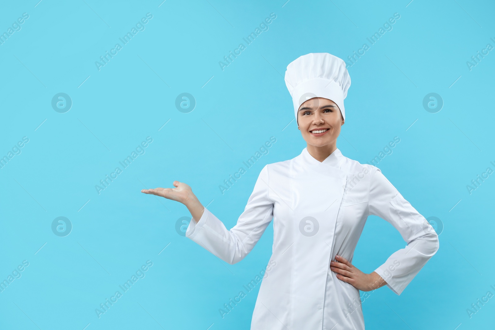 Photo of Happy female chef wearing uniform and cap on light blue background. Space for text