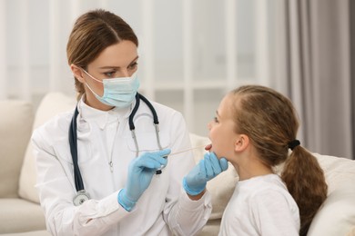 Photo of Doctor in medical mask examining girl`s oral cavity with tongue depressor indoors