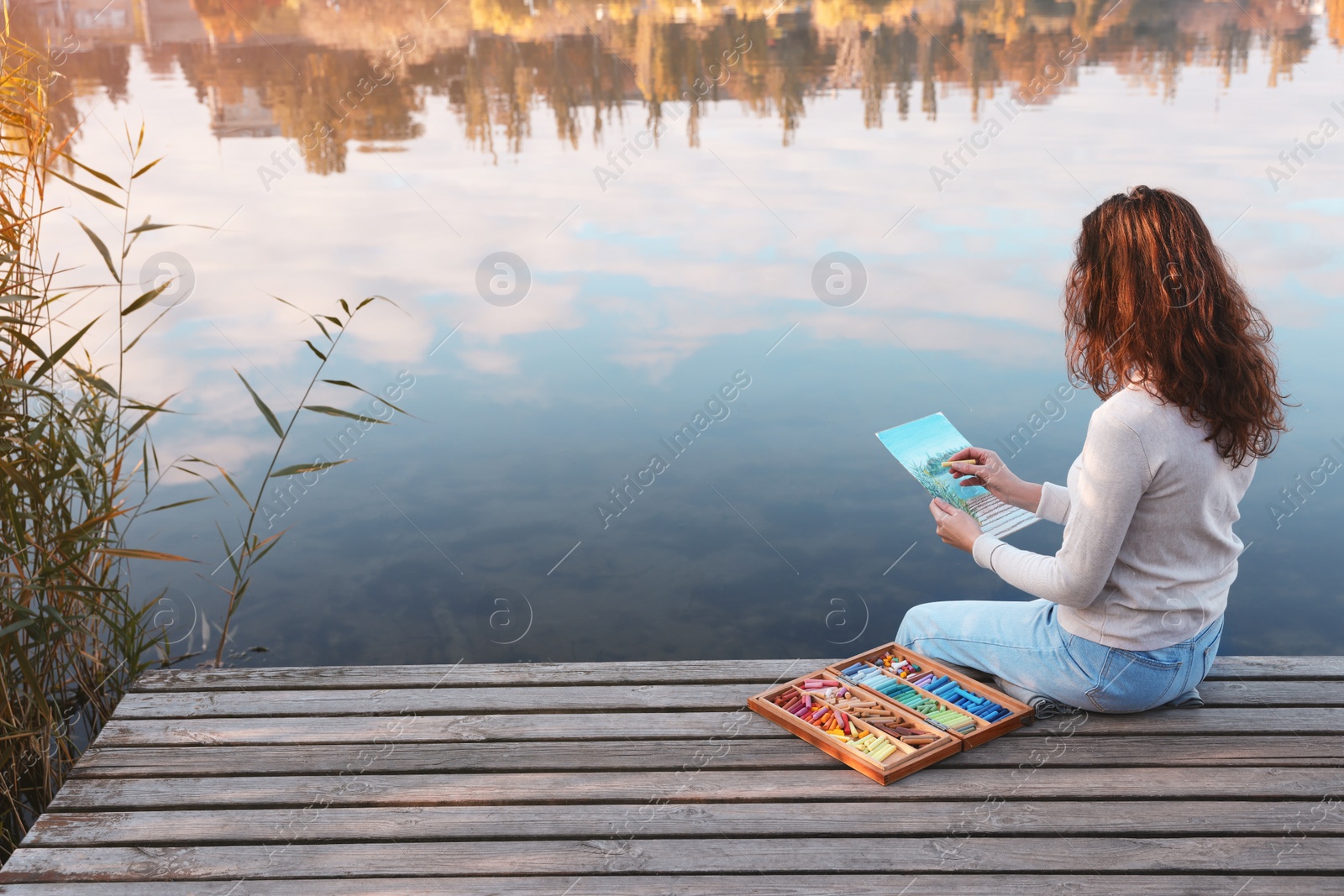 Photo of Woman drawing with soft pastels on wooden pier near water