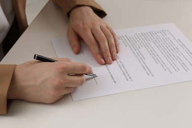 Photo of Businesswoman signing contract at white table, closeup of hands