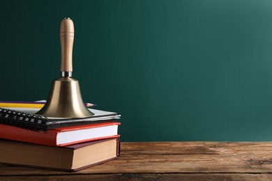 Golden bell, books and pencils on wooden table near green chalkboard, space for text. School days