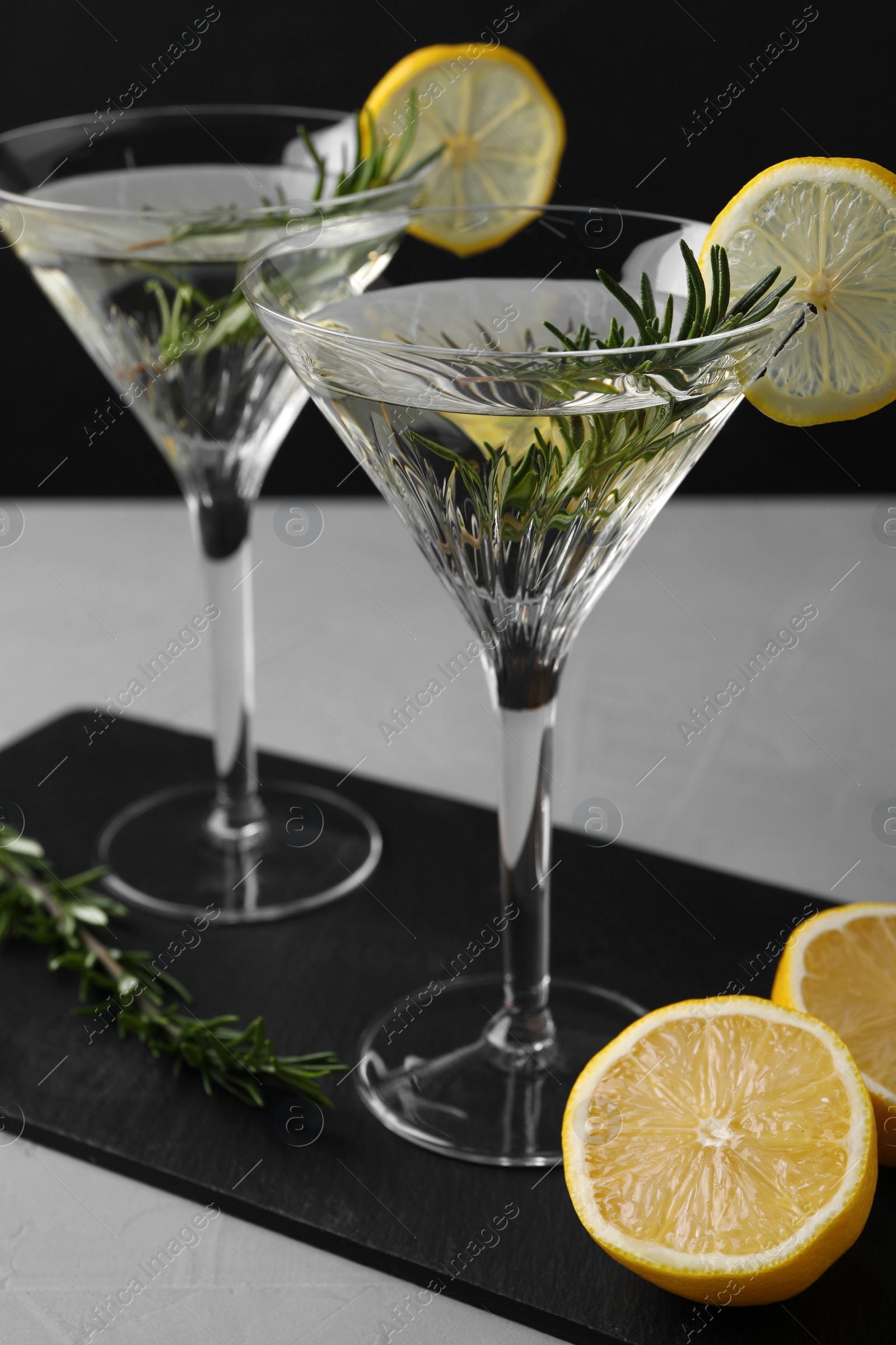 Photo of Martini glasses of refreshing cocktail decorated with lemon slices and rosemary on grey textured table